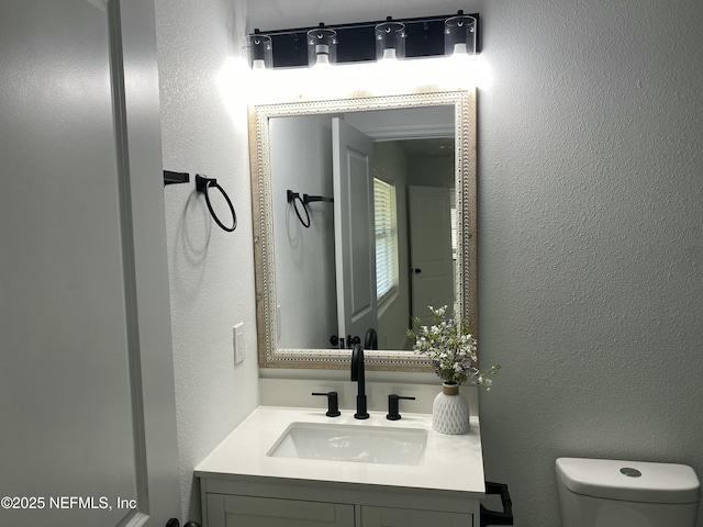 half bathroom featuring a textured wall, vanity, and toilet