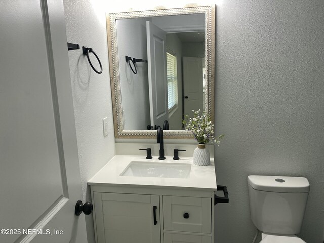 half bath featuring a textured wall, vanity, and toilet