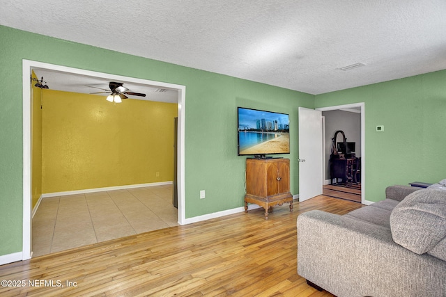 living area with light wood-style floors, a textured ceiling, baseboards, and ceiling fan
