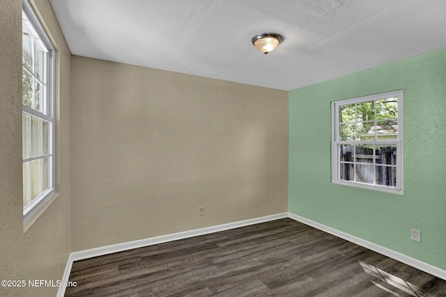spare room featuring baseboards, a textured wall, and dark wood-type flooring