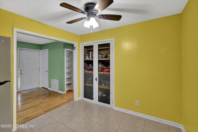 empty room with a textured wall, a textured ceiling, a ceiling fan, and baseboards