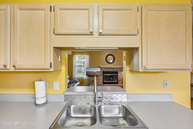 kitchen featuring light brown cabinetry, a premium fireplace, light countertops, and a sink