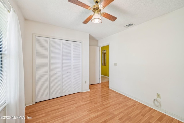 unfurnished bedroom featuring a textured ceiling, visible vents, light wood-style floors, a closet, and baseboards