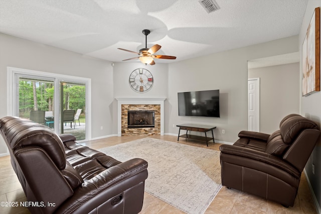 living area featuring a fireplace, baseboards, visible vents, a ceiling fan, and a textured ceiling