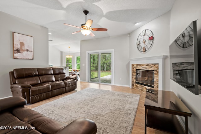 living area featuring a textured ceiling, ceiling fan, light wood-style floors, baseboards, and a fireplace