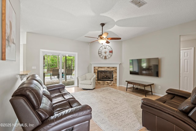 living room with a textured ceiling, visible vents, ceiling fan, and a fireplace