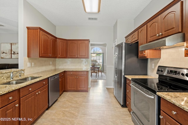 kitchen with light stone counters, stainless steel appliances, under cabinet range hood, a sink, and visible vents