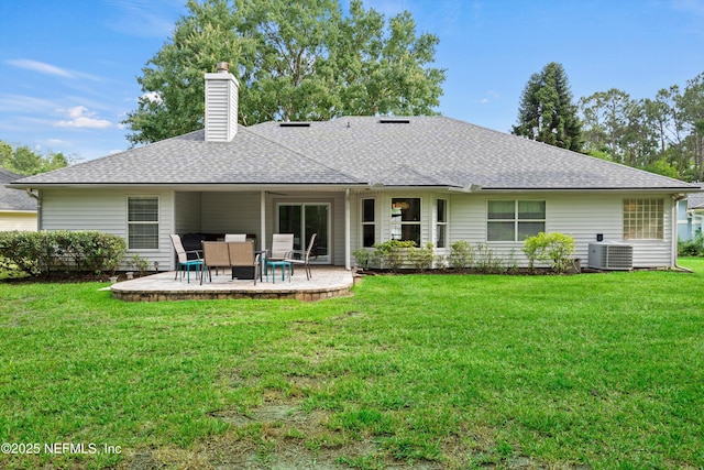 rear view of house with a patio, a chimney, roof with shingles, a lawn, and central AC