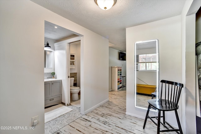 hall featuring baseboards, light wood finished floors, and a textured ceiling