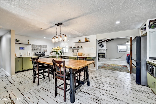 dining room featuring light wood-style flooring, a stone fireplace, ceiling fan with notable chandelier, and a textured ceiling