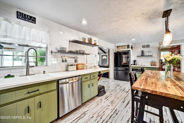 kitchen with a textured ceiling, visible vents, appliances with stainless steel finishes, a sink, and green cabinets