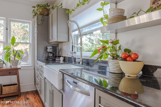 kitchen featuring light wood-style floors, baseboards, dark stone countertops, dishwasher, and gray cabinetry