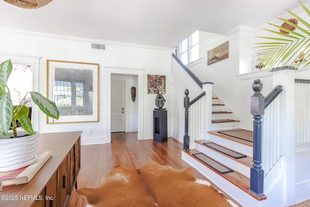 entryway featuring visible vents, wood finished floors, baseboards, ornamental molding, and stairs