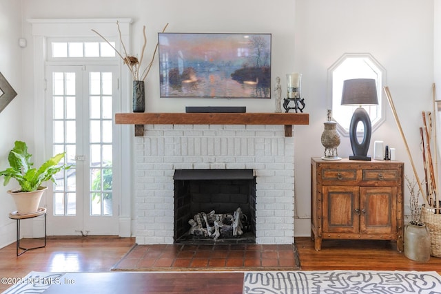 living area with a brick fireplace, french doors, and wood finished floors