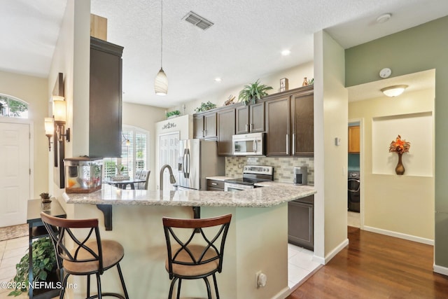 716 Hazelmoor Ln, Ponte Vedra, FL 32081 - kitchen with visible vents, a peninsula, dark brown cabinetry, a kitchen bar, and stainless steel appliances