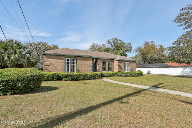 ranch-style home featuring brick siding, fence, and a front lawn