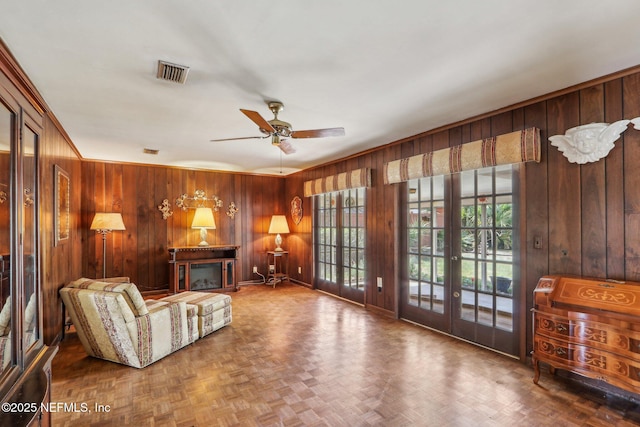 living area featuring visible vents, a ceiling fan, wood walls, and plenty of natural light