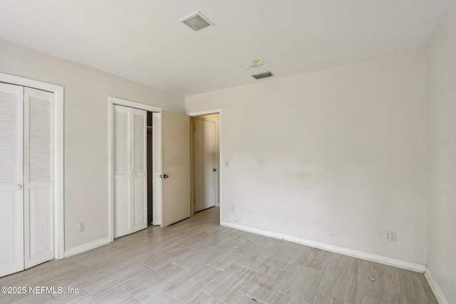 unfurnished bedroom featuring visible vents, two closets, light wood-style floors, and baseboards