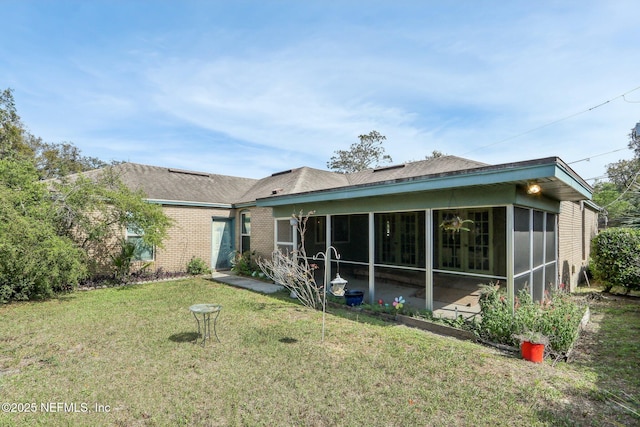 rear view of property with a yard, brick siding, and a sunroom
