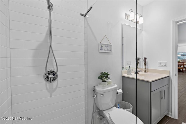 bathroom featuring wood finished floors, toilet, vanity, and tiled shower