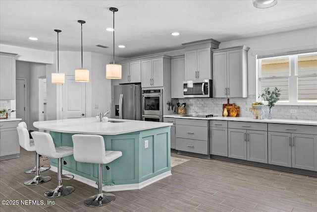 kitchen featuring a sink, light wood-style floors, backsplash, gray cabinets, and appliances with stainless steel finishes