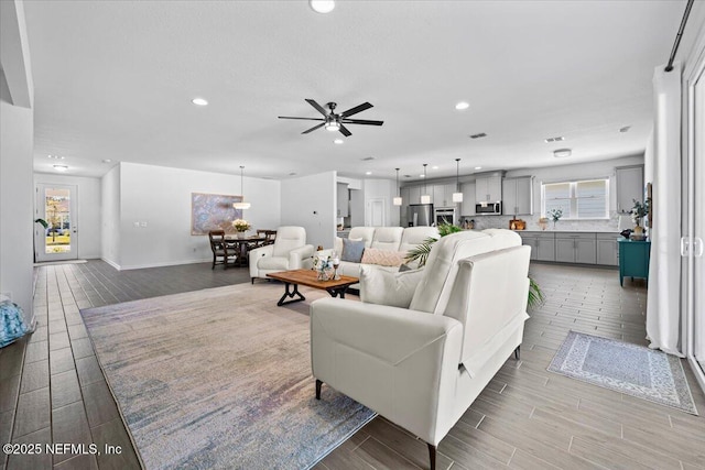 living area with plenty of natural light, a ceiling fan, wood finished floors, and baseboards