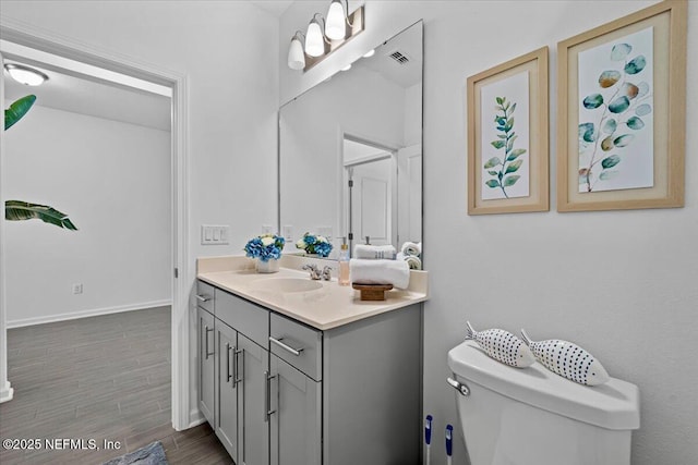 bathroom featuring wood finished floors, visible vents, toilet, vanity, and baseboards