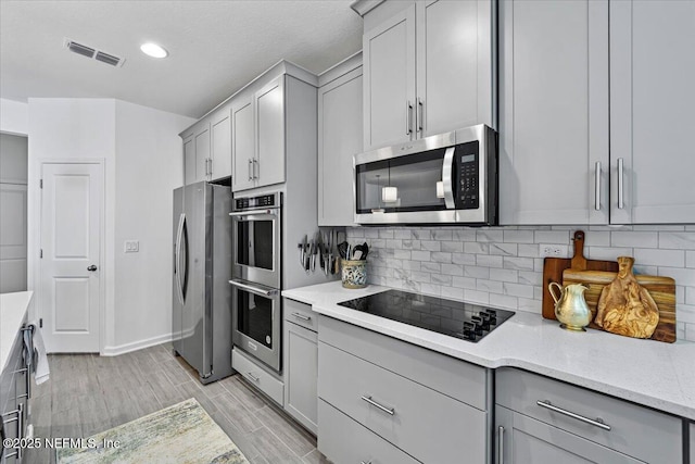 kitchen with wood tiled floor, gray cabinets, stainless steel appliances, backsplash, and visible vents