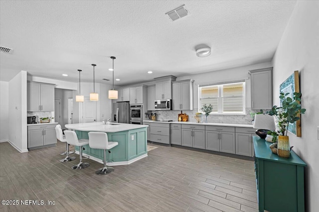 kitchen with backsplash, a kitchen bar, stainless steel appliances, and gray cabinetry