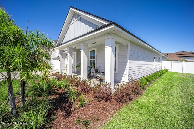 view of home's exterior with a lawn, fence, a porch, and board and batten siding