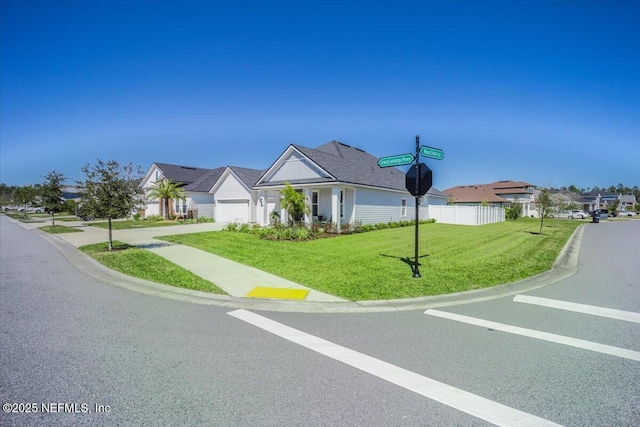 view of front facade featuring fence, an attached garage, a front lawn, and a residential view