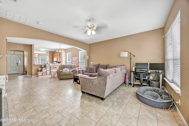 living room with arched walkways, ceiling fan with notable chandelier, baseboards, visible vents, and light tile patterned flooring