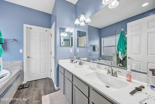 full bath with a garden tub, double vanity, a sink, and wood finished floors