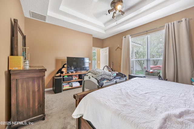 carpeted bedroom featuring a ceiling fan, visible vents, baseboards, and a tray ceiling