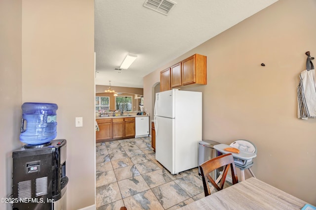 kitchen with white appliances, brown cabinetry, stone finish flooring, visible vents, and a textured ceiling