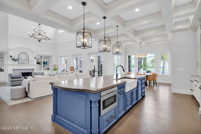 kitchen with a sink, stainless steel microwave, a chandelier, blue cabinets, and coffered ceiling