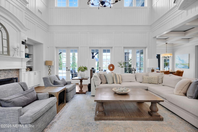 living room featuring a high ceiling, an inviting chandelier, a fireplace, french doors, and wood finished floors