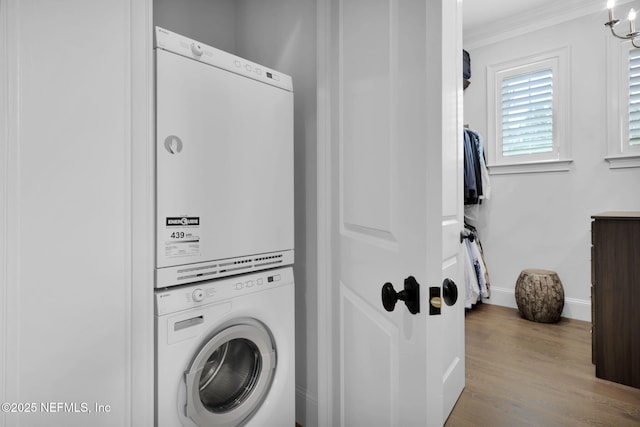 laundry room featuring crown molding, laundry area, stacked washing maching and dryer, baseboards, and wood finished floors