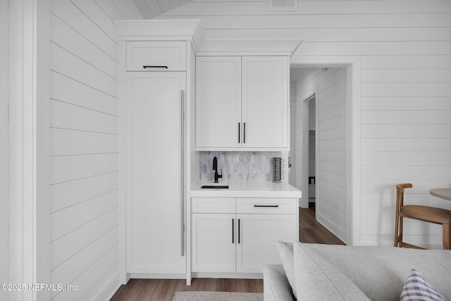 interior space featuring a sink, wood walls, decorative backsplash, and wood finished floors
