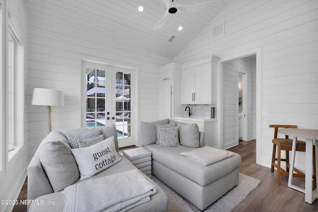 living area featuring a ceiling fan, french doors, dark wood-style flooring, vaulted ceiling, and wooden walls