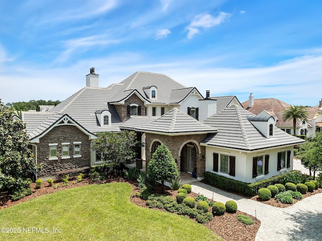 view of front of house with a tile roof, stone siding, stucco siding, a front yard, and a chimney