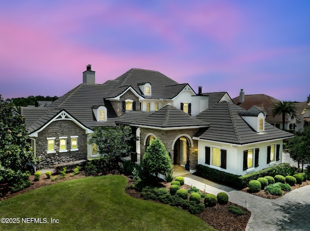 view of front of home featuring a chimney, a front yard, stucco siding, and stone siding