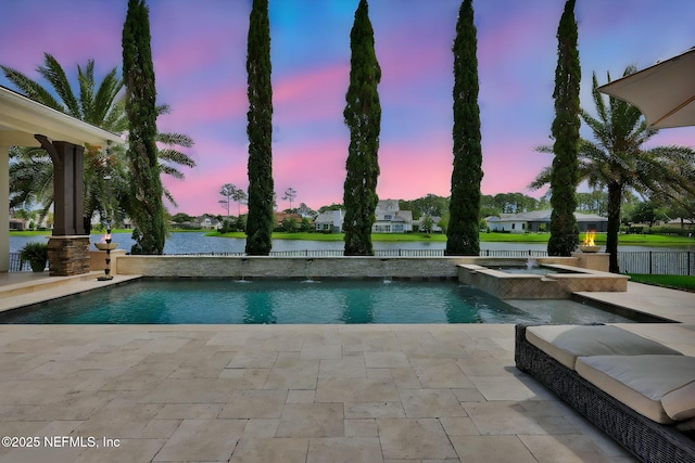 pool at dusk featuring a patio, a water view, and a pool with connected hot tub