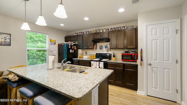 kitchen featuring a kitchen bar, light wood-type flooring, a sink, black appliances, and under cabinet range hood