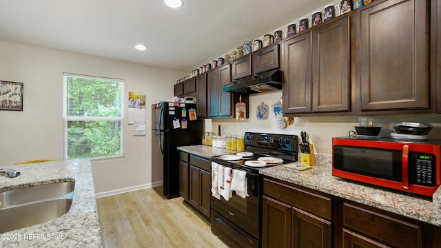 kitchen featuring dark brown cabinets, a sink, light wood-style flooring, under cabinet range hood, and black appliances