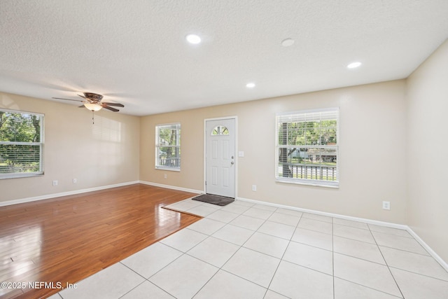 foyer entrance with light wood-style floors, baseboards, ceiling fan, and a textured ceiling