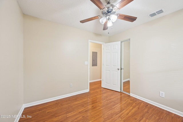 unfurnished bedroom with electric panel, light wood-style flooring, baseboards, visible vents, and a closet