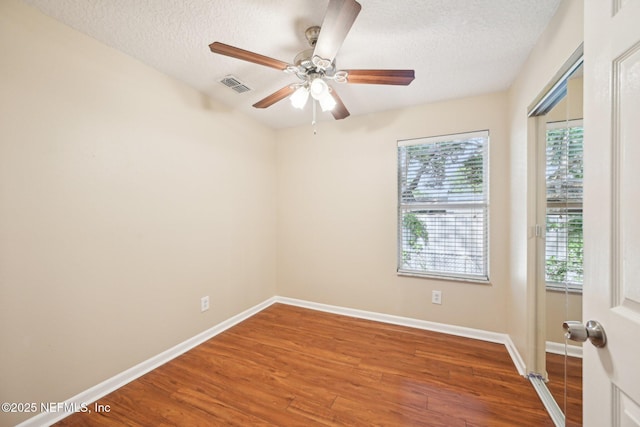 spare room featuring visible vents, baseboards, a textured ceiling, and wood finished floors