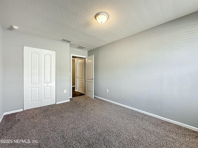 unfurnished bedroom with a textured ceiling, a closet, baseboards, dark colored carpet, and visible vents