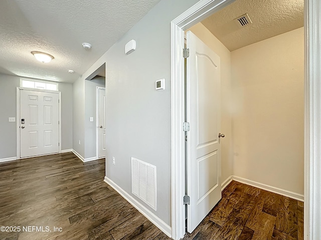 hall featuring dark wood-type flooring, a textured ceiling, and visible vents